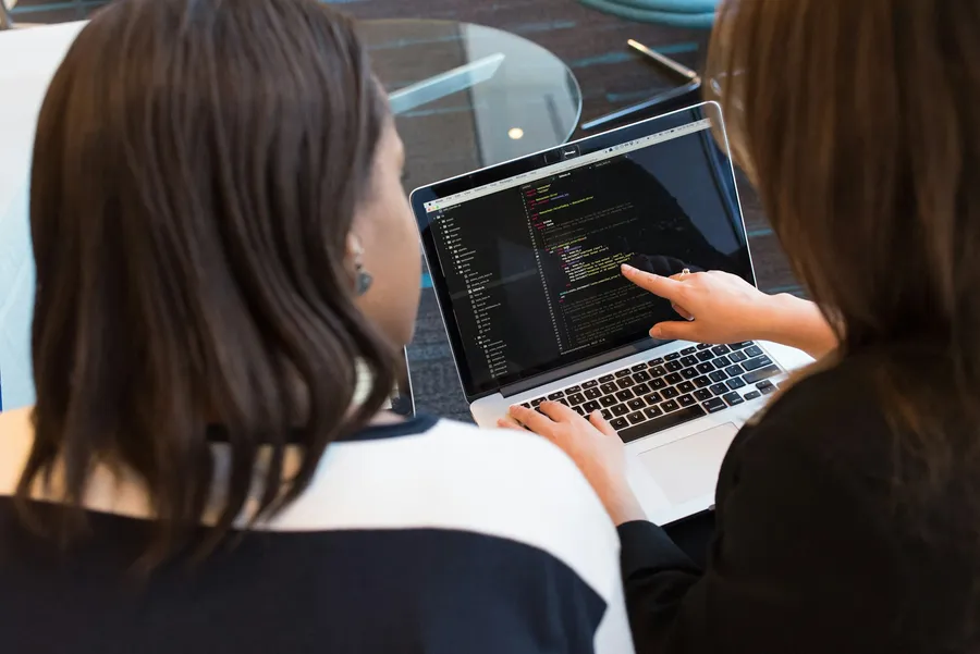 Deux femmes révisent du code sur un ordinateur portable, l'une pointe l'écran