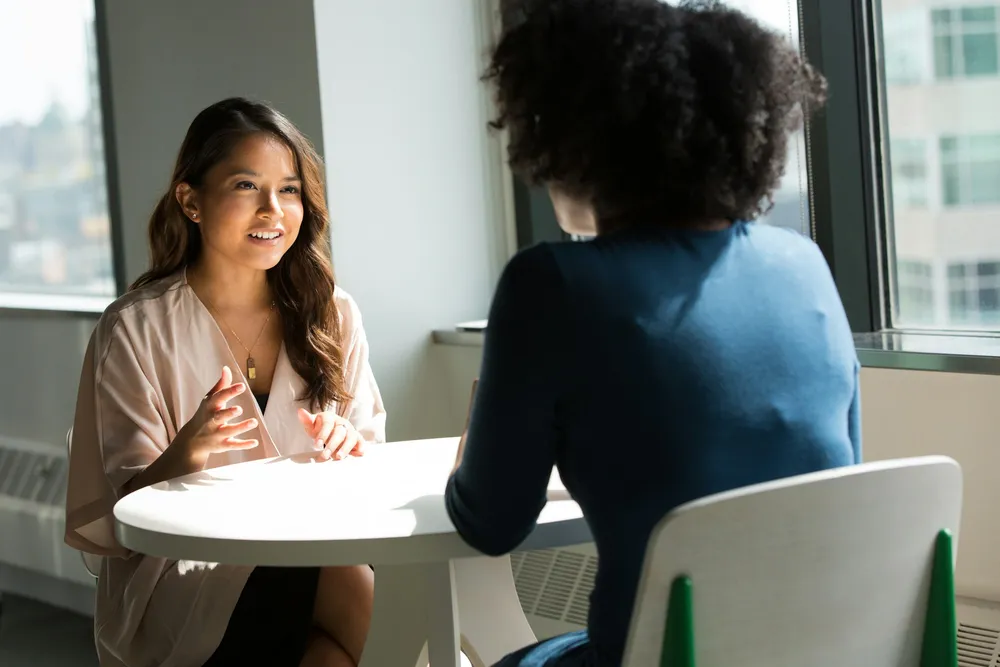 Deux femmes en conversation à une petite table ronde, près d'une fenêtre