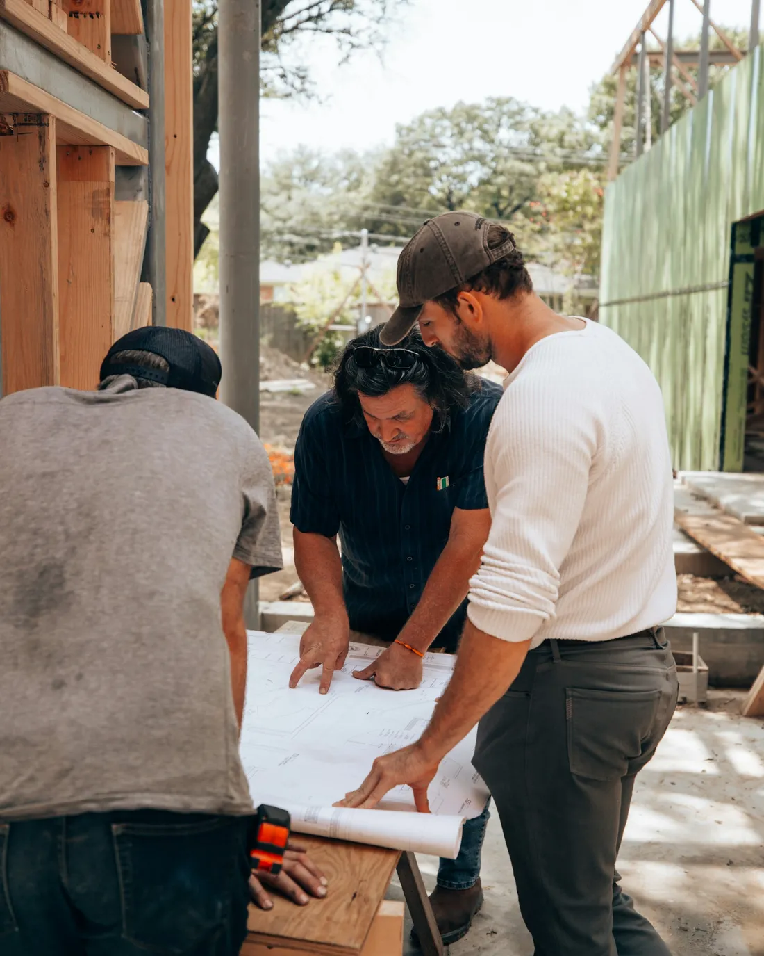 Trois entrepreneurs penchés sur des plans papier dans une maison à ossature de bois en construction